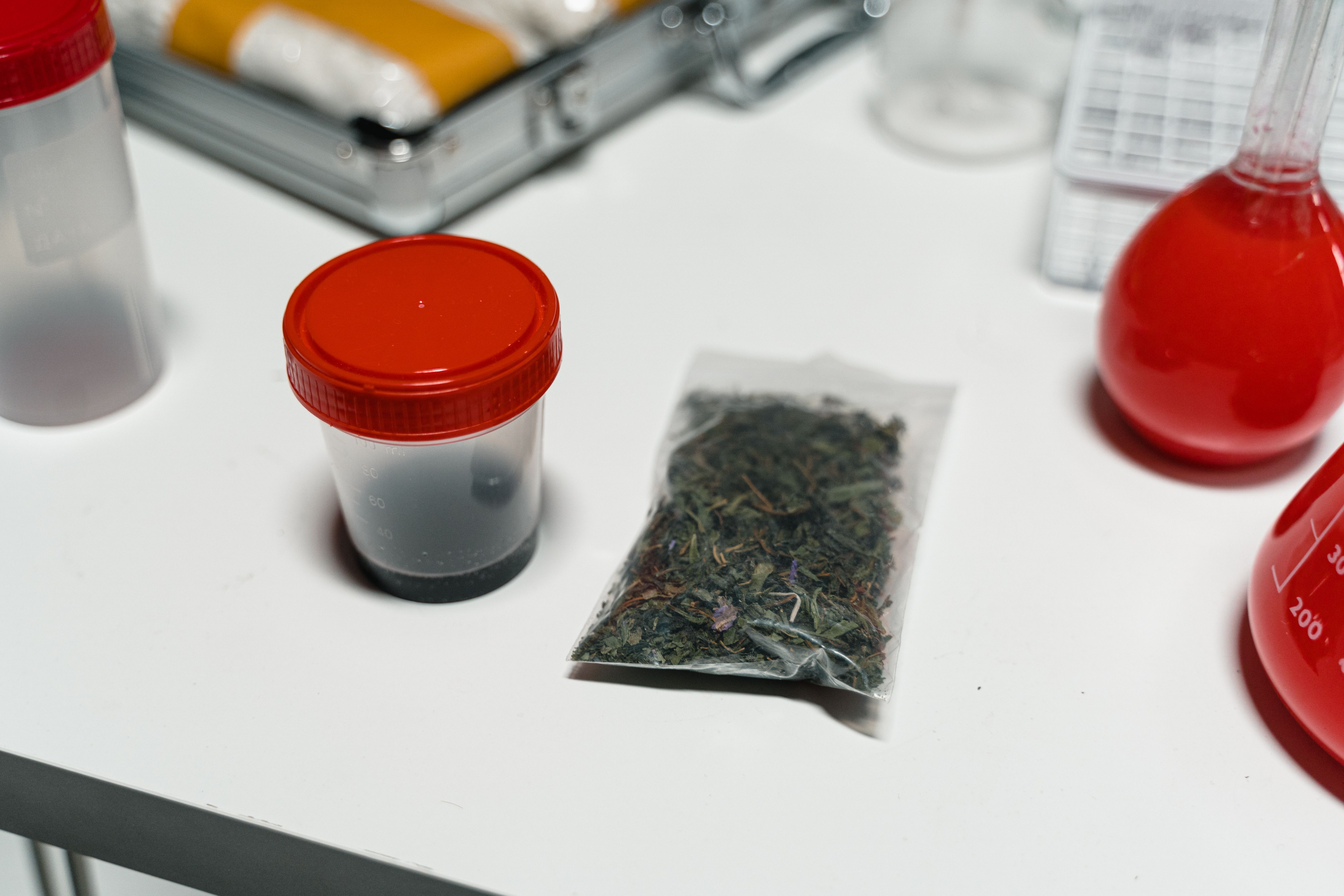 Cannabis packaged in a plastic bag and containers with red lids on a white surface