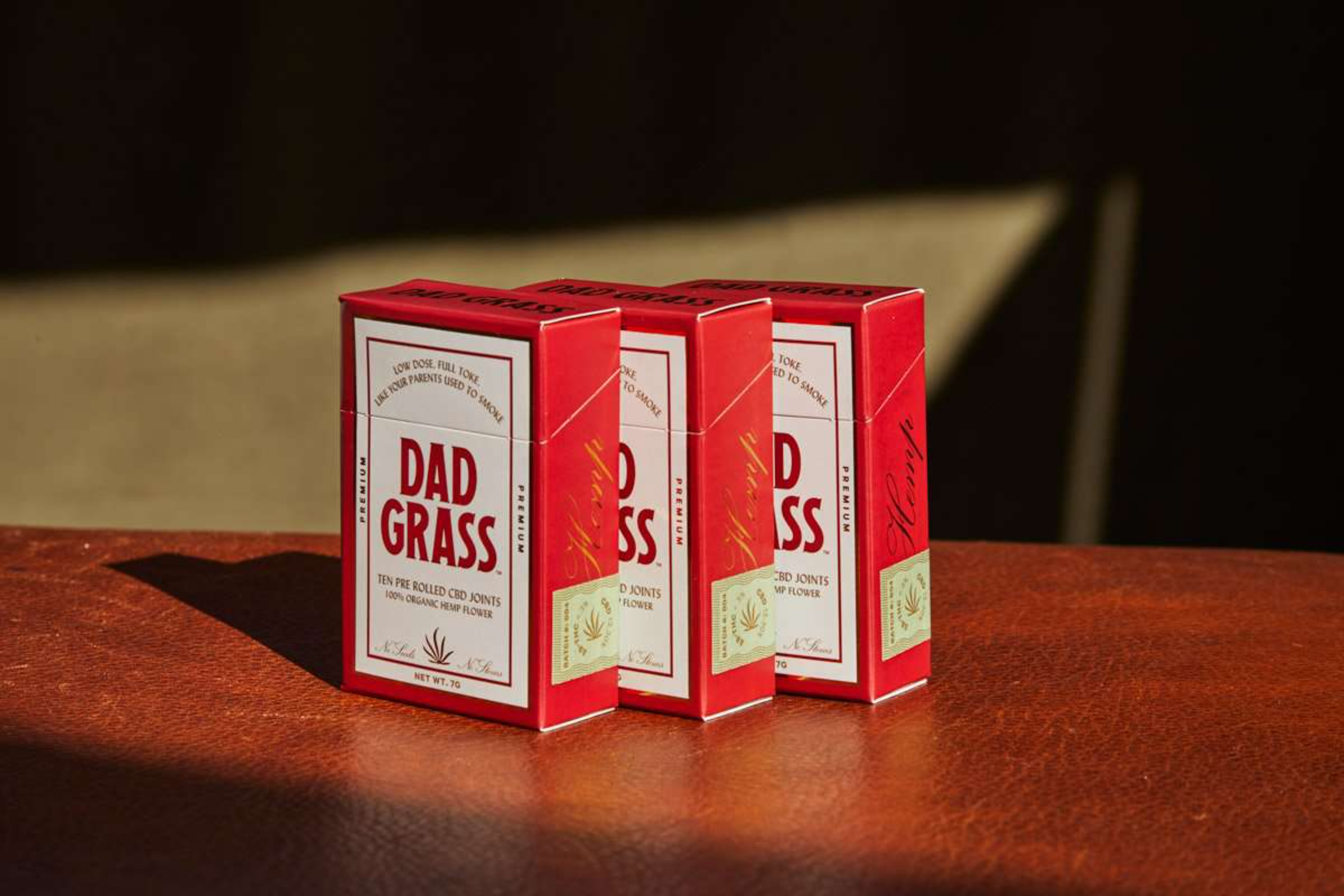 Three branded red CBD joint boxes placed on a leather surface in natural light