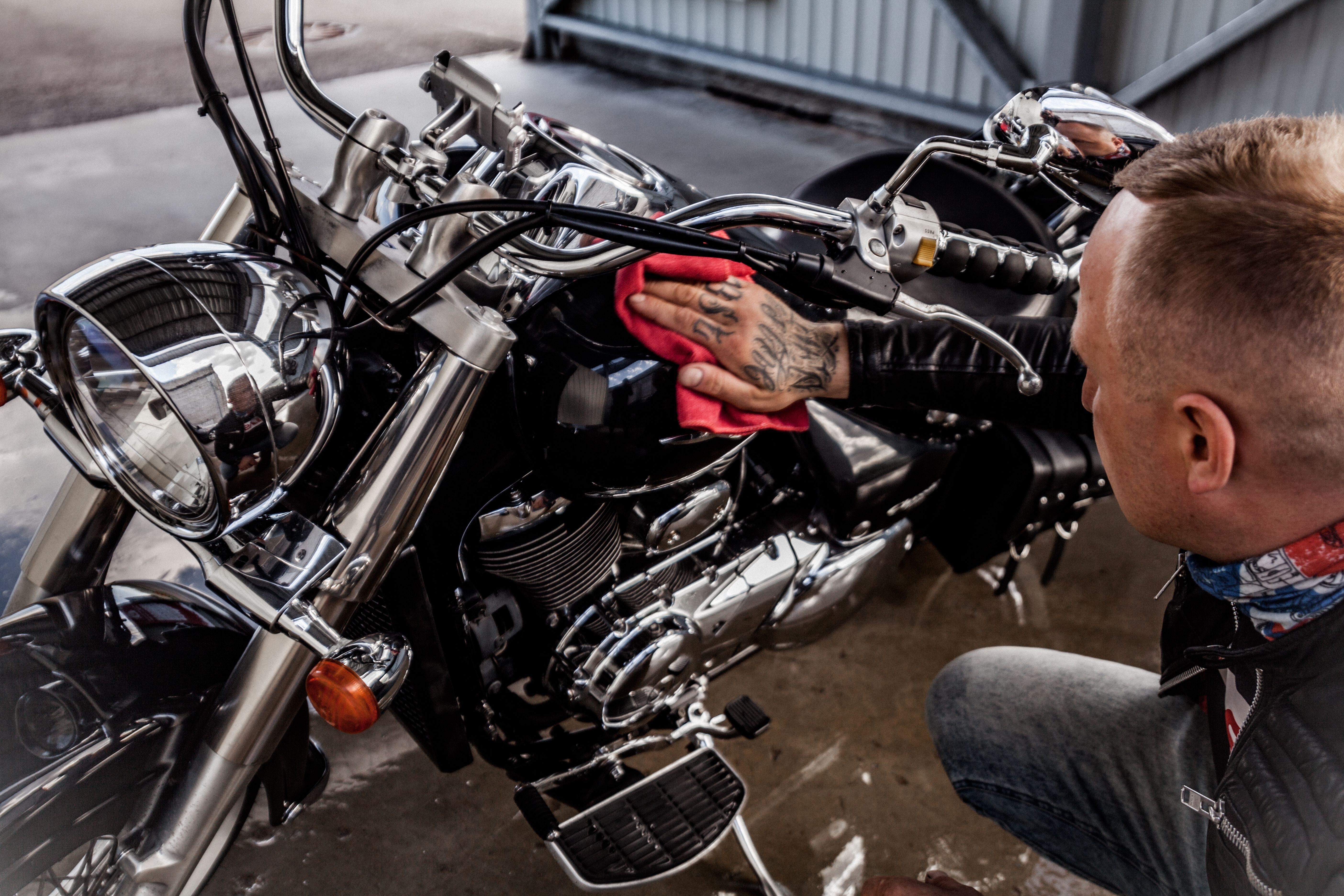 Man polishing a shiny motorcycle with a red microfiber cloth indoors