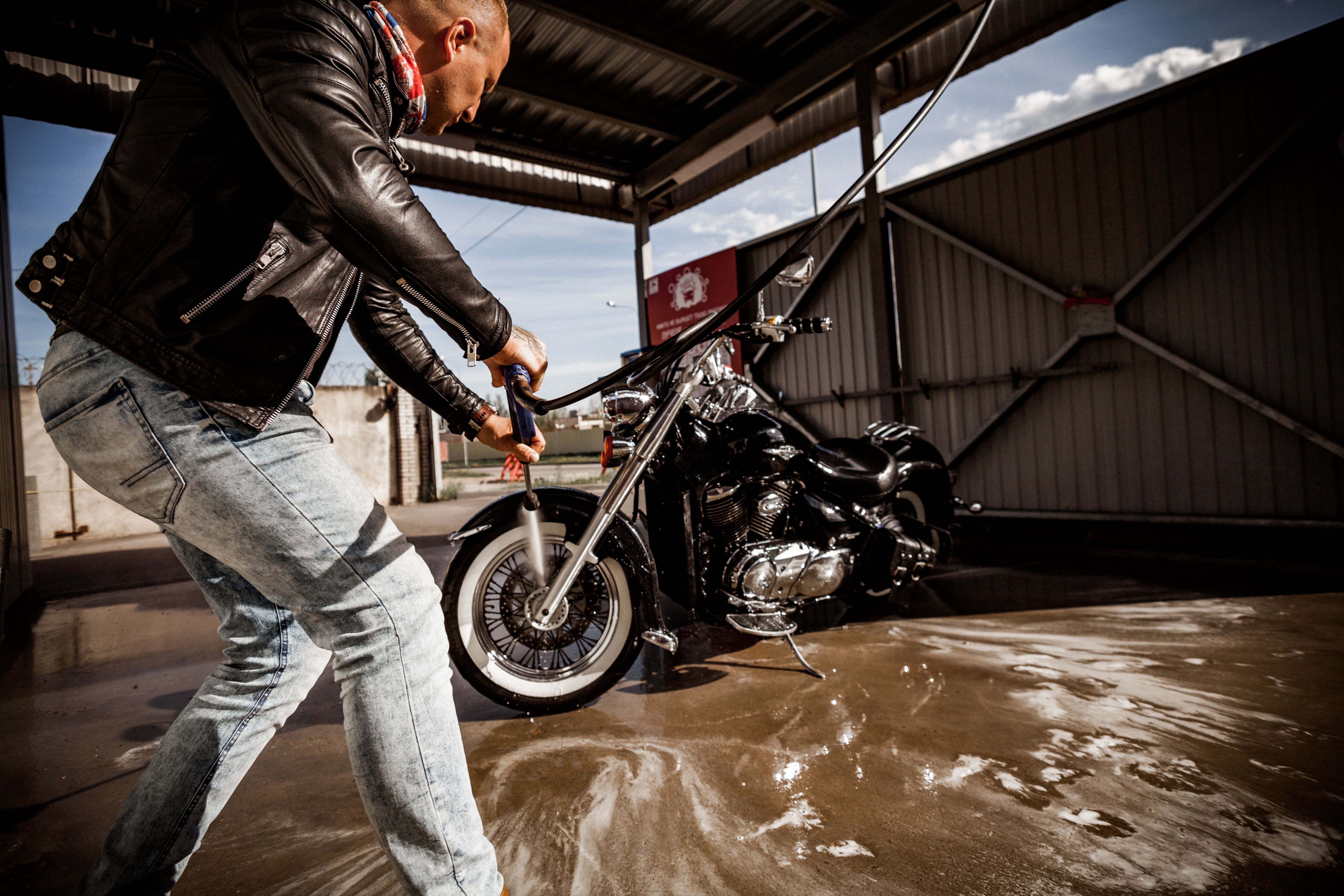 Man rinsing and cleaning a motorcycle with a hose at an outdoor wash station