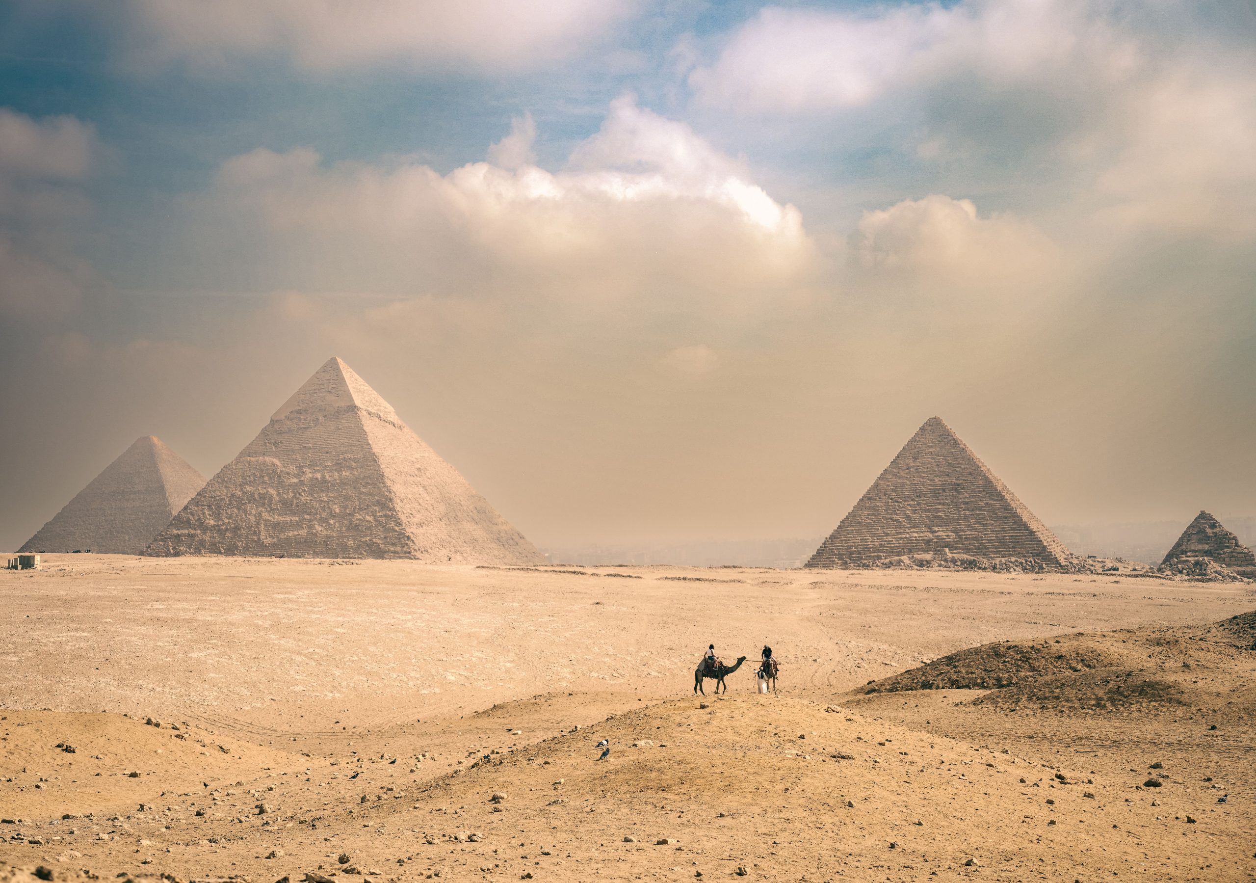 Pyramids of Giza under a sunny sky with travelers riding camels in the Egyptian desert