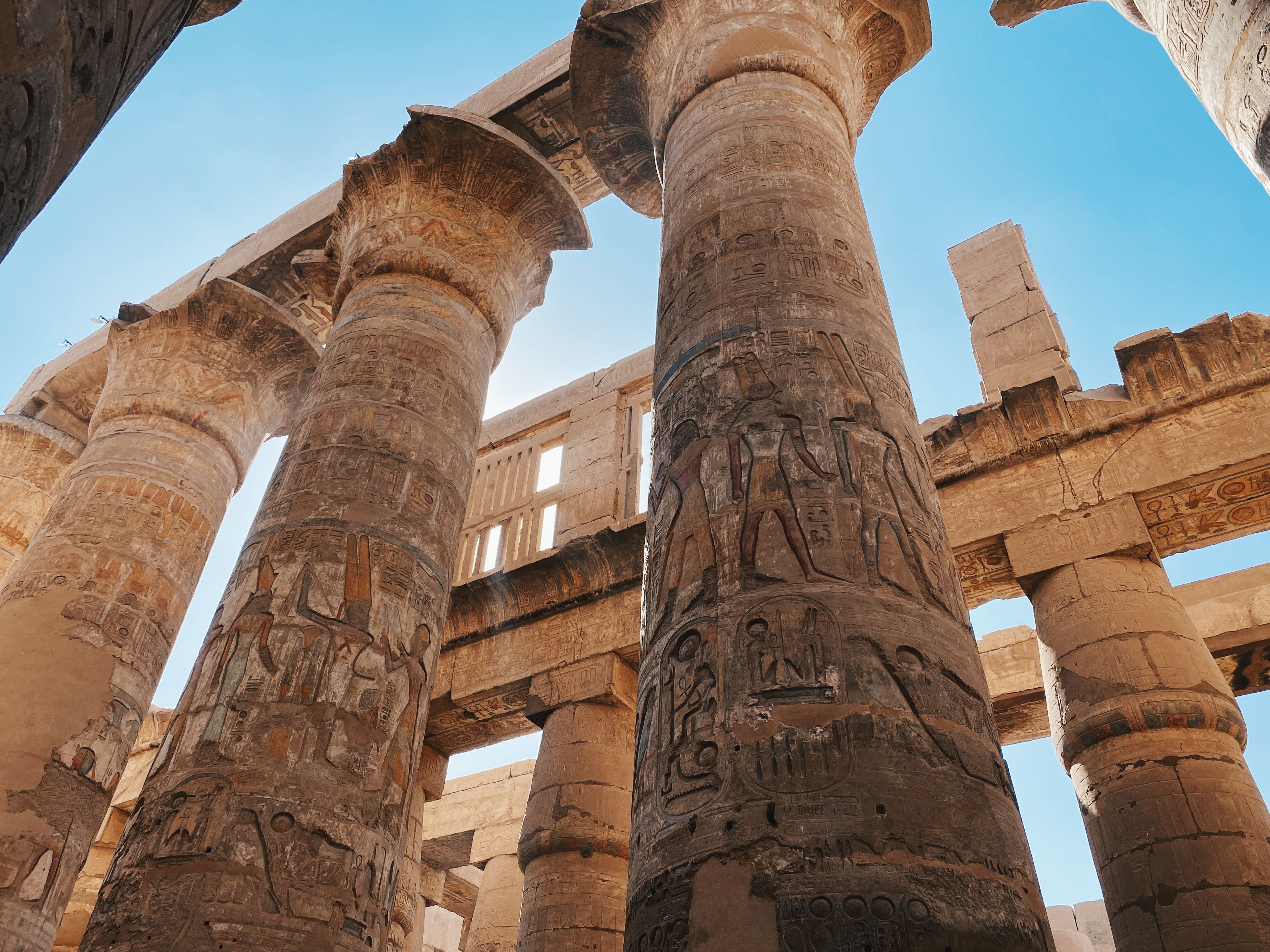 Ancient Egyptian temple columns covered in hieroglyphics under a clear blue sky