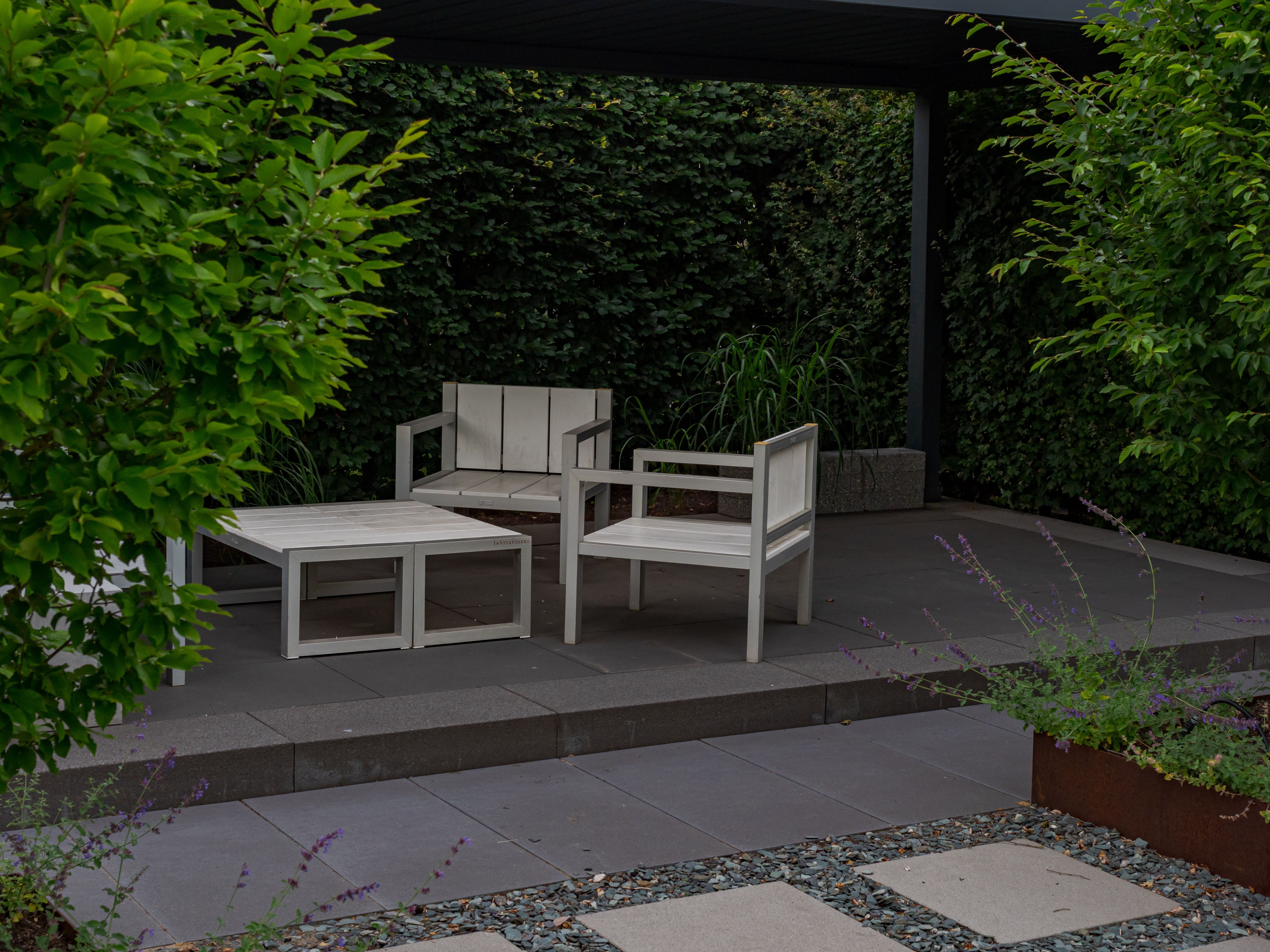 Minimalist wooden patio furniture surrounded by lush planting, combining modern backyard design with a natural setting.